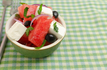 Summer salad with watermelon, feta cheese, olives and mint in a green bowl on a green napkin. Concept of healthy eating. Vegan, vegetarian. Horizontal orientation. Copy space