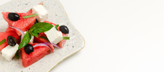 Summer salad with watermelon, feta cheese, olives and mint in a white plate on a white table. Concept of healthy eating. Vegan, vegetarian. Horizontal orientation. Top view. Banner