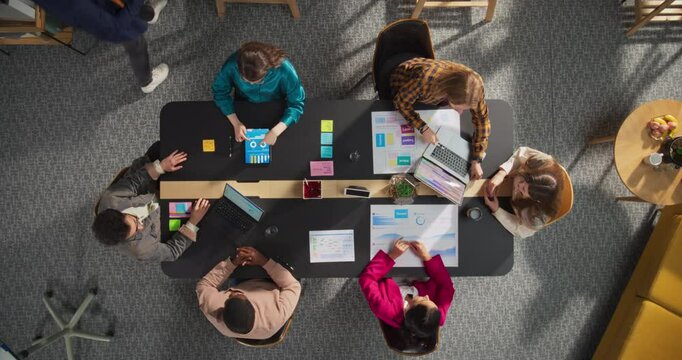 Top Down View: Diverse and Creative Colleagues Working Together At The Conference Table In Stylish Office. Male And Female Business People Using Tablets, and Laptops To Analyze Business Data On Charts