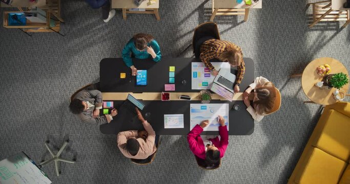 Top Down View of Young, Diverse Entrepreneurs in a Colorful Office, Solving Problems and Designing Software, Using laptop, Tablets, and Creative New Project at Conference Table. Productive Teamwork