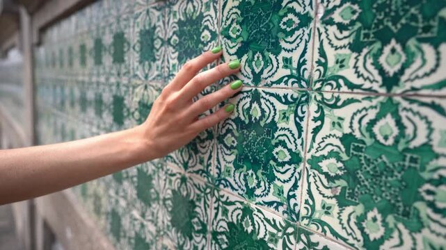 girl tourist walks along old Porto street touching green nailed hand wall with green azulejo tiles, close view