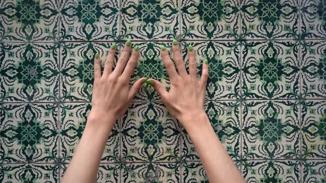 green nailed hands touching wall with green azulejo tiles, close view