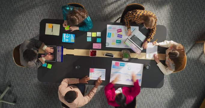 In the Startup Meeting Room: Team of Entrepreneurs Sitting at the Conference Table, Discussing Business, Solving Problems, Using Tablet, Laptop, Sharing Documents. Top Down View Time Lapse Shot.