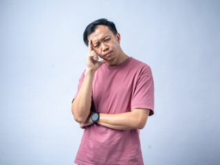 A man in a pink shirt looks thoughtfully upwards with his hand on his chin, reflecting a pensive...
