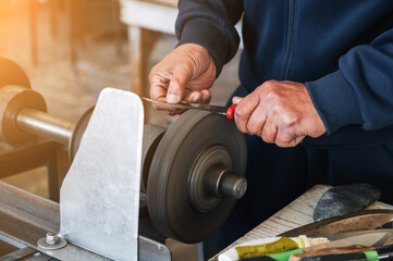hands of a male sharpener grinder sharpening knife blade on a sharpening machine in outdoor