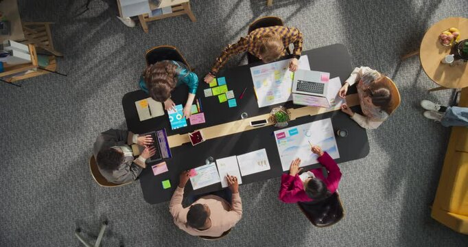Top Down View Of Creative Startup Office Meeting Room: Diverse Coworkers Using Laptop Computers At the Conference Table, Discussing Ideas, Brainstorming New Strategies. Corporate Workspace Concept. - Powered by Adobe
