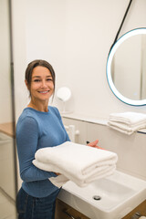 Dark-haired woman holding a pile of white towels in hands