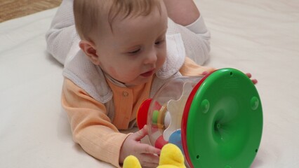 Adorable happy blonde infant baby playing with kids toys at home while sitting on carpet floor in living room. Portrait of smiling cute child toddler using colorful toys, copy space