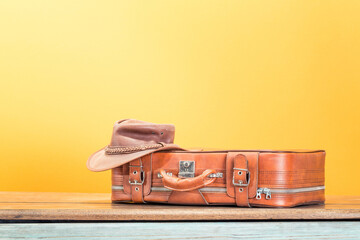 Vintage old classic traveler valise and leather cowboy hat front yellow wall background. Travel...