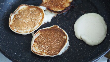 Housewife woman bakes pancakes for breakfast and pours dough into hot frying pan. Homemade pancakeson glass-ceramic stove in kitchen. Ingredients for making pancakes. Selective focus.