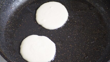 Housewife woman bakes pancakes for breakfast and pours dough into hot frying pan. Homemade pancakeson glass-ceramic stove in kitchen. Ingredients for making pancakes. Selective focus.