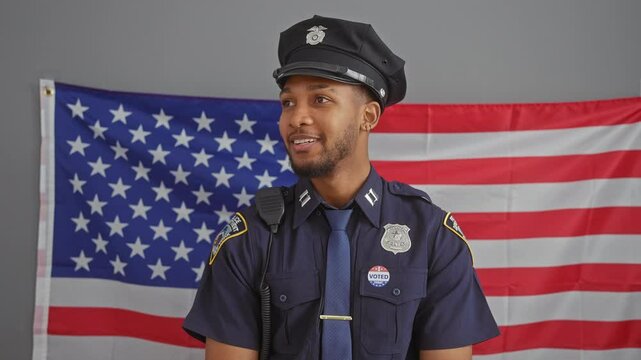 A confident african american male police officer stands before an american flag, badge and radio visible, embodying service and patriotism.