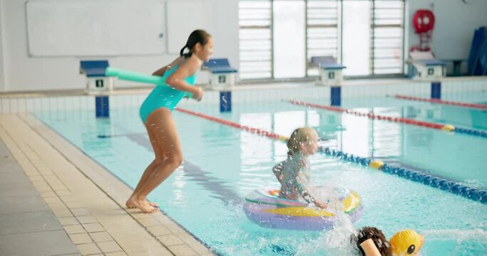 Kids, happy and jump in swimming pool with floatie for lesson in centre with swimsuits for recreation. People, friends and diversity with smile or excited for workout and training with sport
