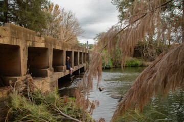 Teen boy sitting under low bridge over the Cudgegong River in rural New South Wales
