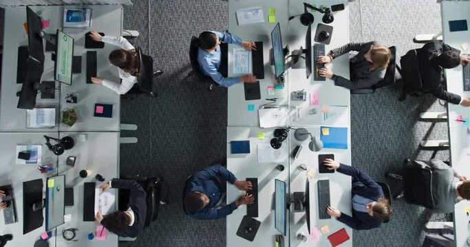 Top Down View of Multiethnic Team in a Corporate Office, Working on Desktop Computers And With Financial Documents. Colleagues Working Creating Reports, Developing Business Strategies For Hedge Fund.