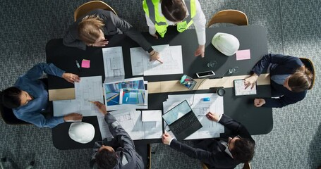 Top Down View of Diverse Team of Real Estate Construction Engineers Discussing Blueprints, Documents in a Corporate Office. Modern Workspace of Architectural Buro With Colleagues Using Tablet, Laptop.