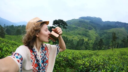 Traveler fascinated tea plantations Sri Lanka, takes selfie while enjoying cup aromatic brewed tea. Selfie emerald leaves and female smile. Woman shares selfie, inviting journey through tea region.