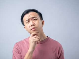 A man in a pink shirt looks upwards with a confused and puzzled expression, his eyebrows raised and mouth slightly open. The plain light blue background emphasizes his bewildered demeanor.