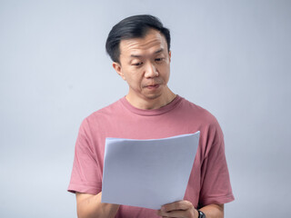 A man in a pink shirt looks excitedly at a stack of papers he is holding, his mouth open in...