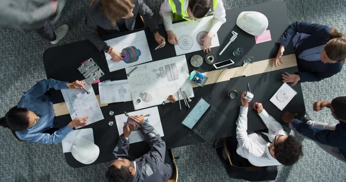 Zoom Out Top Down View: Diverse Team of Business Managers and Construction Engineers Working With Blueprints Of Heavy Industrial Machinery in An Office. Teamwork Of Colleagues With Laptop, Tablet