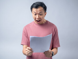 A man in a pink shirt looks excitedly at a stack of papers he is holding, his mouth open in...