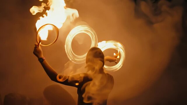 Skilled performer twirls flaming batons, creating mesmerizing circles of fire against dark backdrop. Intense orange glow illuminates artist's silhouette.