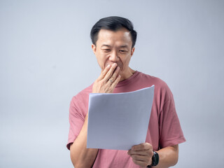 A man in a pink shirt looks excitedly at a stack of papers he is holding, his mouth open in...