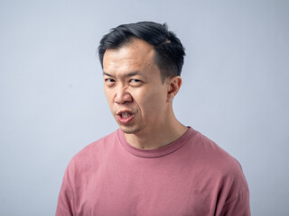 An Asian man in a pink shirt makes a skeptical and uncomfortable expression, as if reacting to something unpleasant. The plain light blue background highlights his displeased