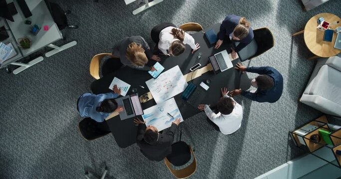 Top Down View Of Diverse Team Of Business Specialists And Managers With Laptops Entering The Conference Room And Sitting Behind Table To Discuss Financial Data And Sales Reports In Corporate Office.