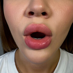 Naklejka premium permanent makeup on the lips of a young woman of a delicate peach shade close-up, a girl after a cosmetic procedure with smooth and clean healthy skin.