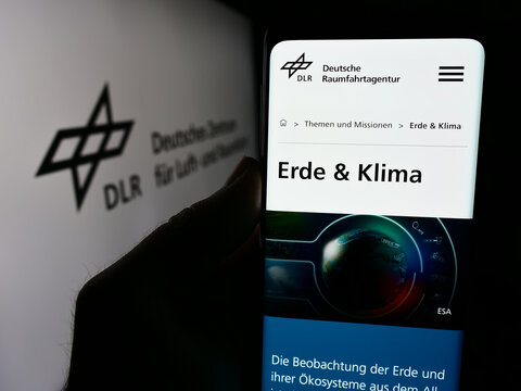 Stuttgart, Germany - 06-26-2024: Person holding cellphone with webpage of Deutsches Zentrum f&uuml;r Luft- und Raumfahrt e.V. (DLR) in front of logo. Focus on center of phone display.