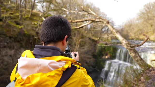 Rear shot of a man filming Sgwd Isaf Clun-Gwyn waterfall in Brecon Beacons National Park, Wales