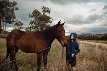 Teen boy standing at farm fence interacting with horses