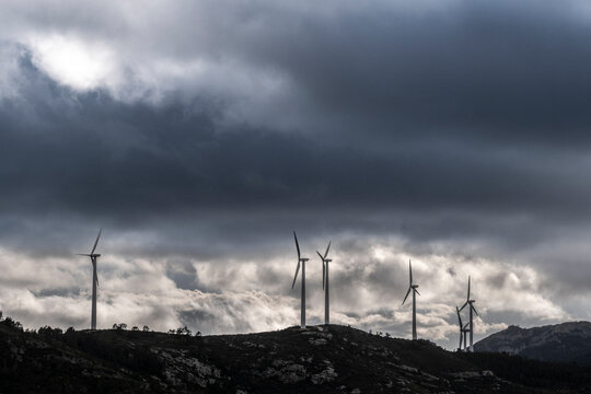 An array of wind turbines stand on a hilltop, highlighted against a dark and stormy sky, symbolizing technological advancement and sustainable energy creation.