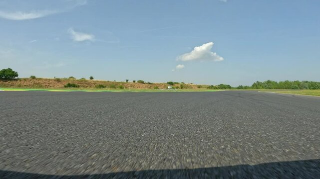 POV: Driving down the empty race circuit in the scenic countryside on a sunny summer day. High speed action shot of driving around the empty winding race track during a fun track day. Motorsport hobby