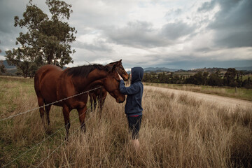 Teen boy standing at farm fence interacting with horses