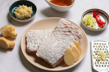 Fresh sea bass fillet with ingredient for delicious steam with soy sauce. Sea bass, soy sauce, ginger grate with a handheld grater, scallion and chili.