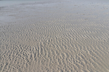 A beautiful beach with white sand and clear water. The sand is rippled from the waves, and the water is calm and inviting.