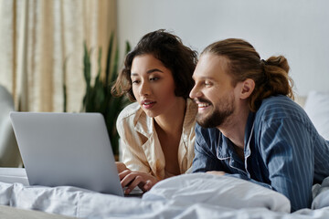 A loving couple relaxing together on a bed, browsing a laptop.
