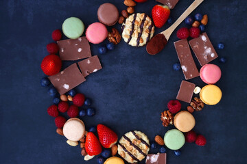 Macarons, chocolate, cookies, berries and various nuts on dark blue background. Top view.