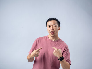 Asian man in a pink t-shirt points at himself with both hands, wearing a confident expression,...