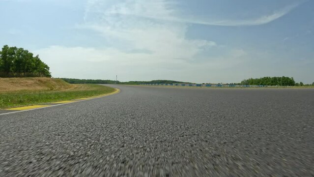 POV: High speed action shot of driving around the empty winding race track during a fun track day. Driving down the empty race circuit in the scenic countryside on a sunny summer day. Motorsport hobby