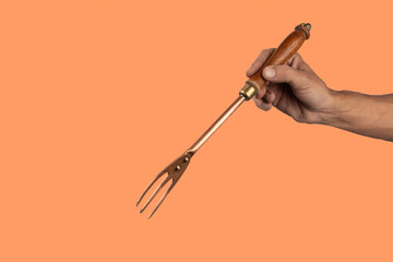 Black male hand holding a vintage brass meat fork on orange background
