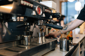 Closeup cropped shot of unrecognizable barista male preparing tasty coffee drink for customer in small business cafe. Making espresso coffee by coffee machine into cup, automated coffeemaker machine.