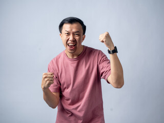 A man in a pink shirt raises both fists in a celebratory gesture, his face beaming with excitement and joy. The plain light blue background emphasizes his triumphant and enthusiastic expression.