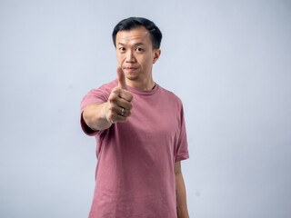 A man in a pink shirt smiles and gives a thumbs-up gesture, exuding positivity and approval. The plain light blue background highlights his cheerful and confident demeanor.