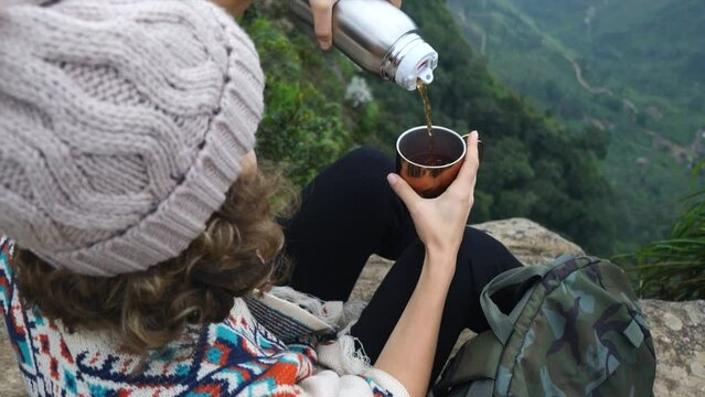 Tourist, sitting on toprock, pours aromatic hot tea from thermos into mug. Every sip hot tea warms and gives feeling comfort against backdrop majestic landscapes. Tea becomes integral part adventure.
