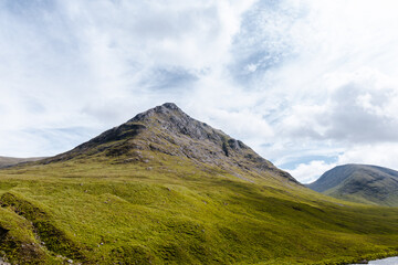 Wide view of Glencoe Valley with a winding river, green mountains, and a bright blue sky filled with fluffy clouds.