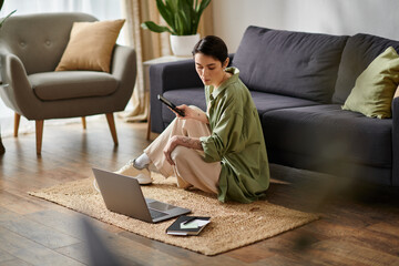 A woman sits on a rug in her living room, working on her laptop.