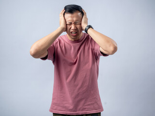 Fototapeta premium A man in a pink shirt holds his head with a pained expression, indicating a headache or discomfort. The plain light blue background emphasizes his distress and highlights his posture and expression.
